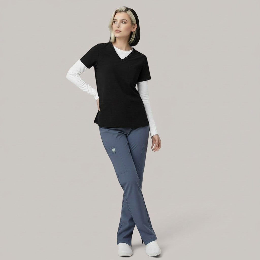 Model wearing Élaura Faye cargo pants in slate blue with a black V-neck scrub top and white long-sleeve base layer.